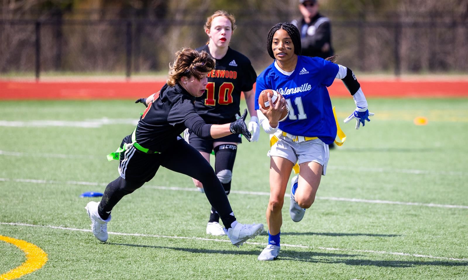 A girl wearing a Nolensville High uniform runs down the field while holding a football.
